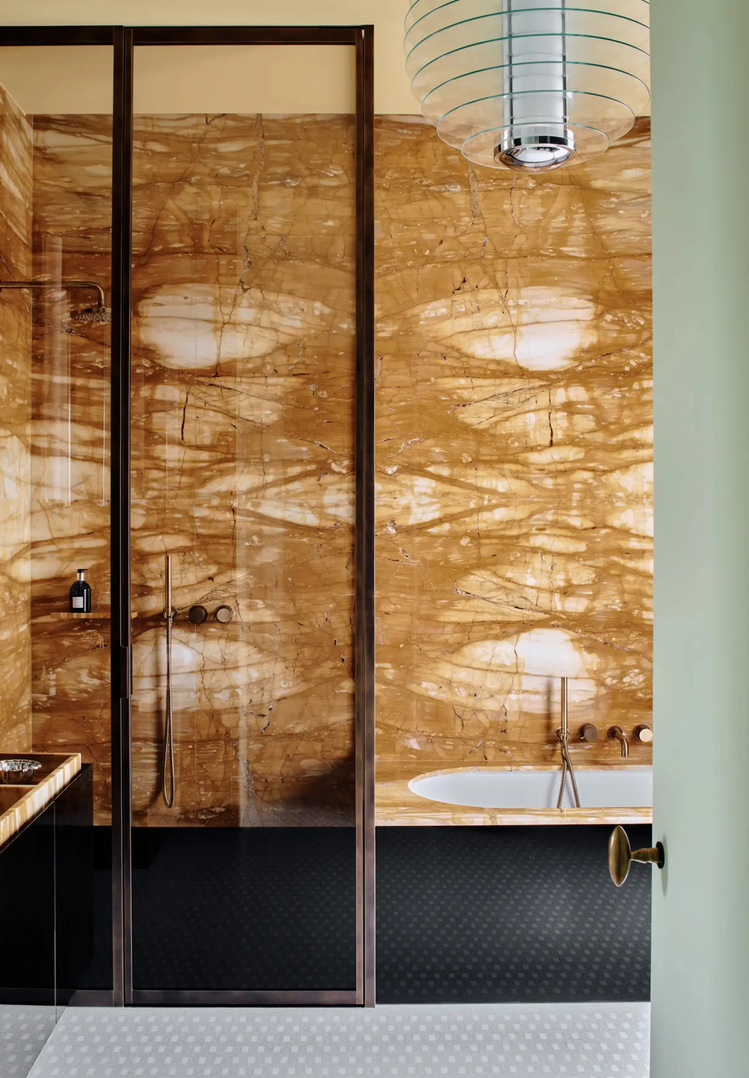 Bagno master in Giallo Siena lucido a macchia aperta con box doccia e profili in bronzo scuro, vasca integrata con rubinetteria in ottone e pavimento in mosaico bianco nel centro storico di Milano – progetto LC Atelier x Trapattoni Marmi