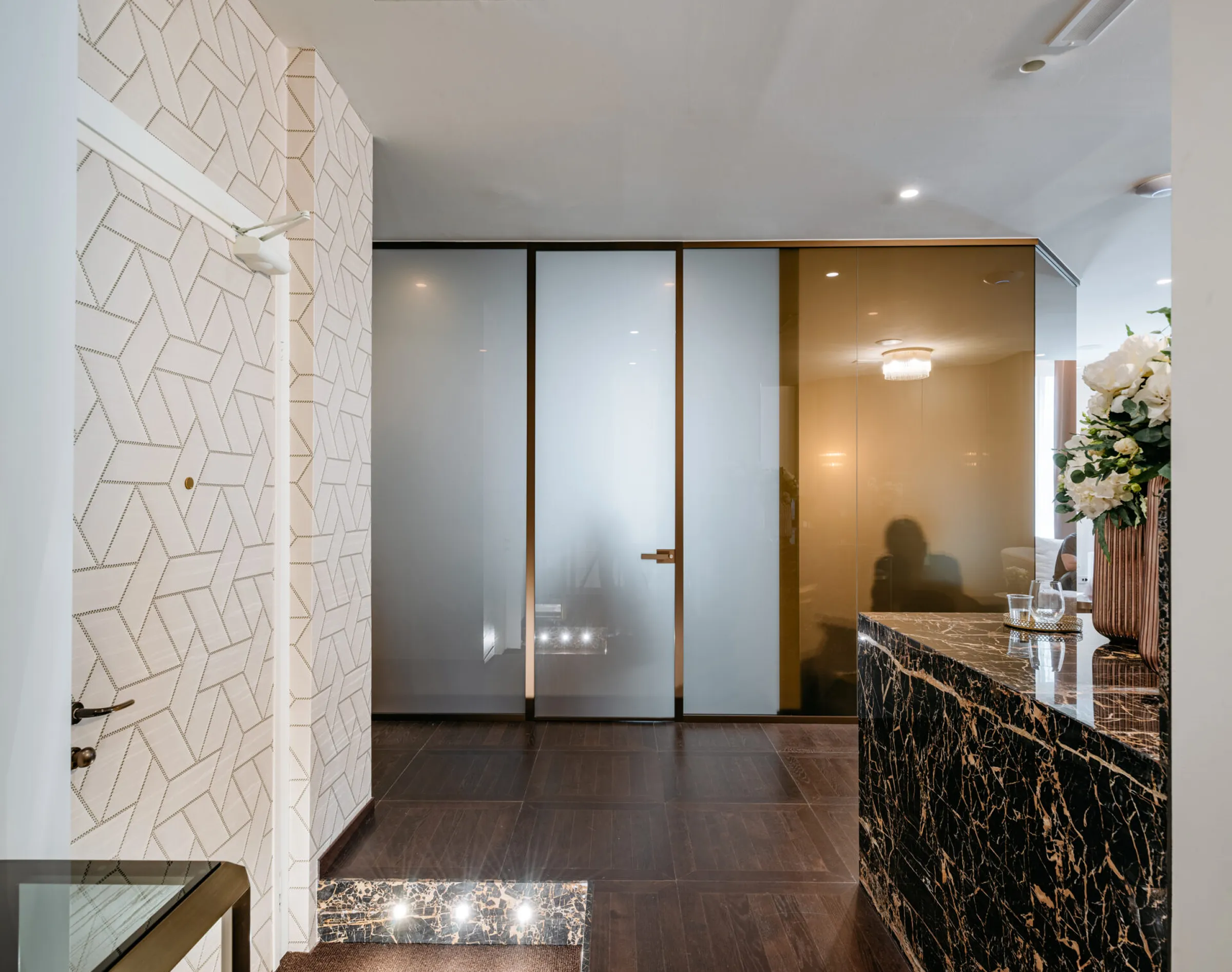 Ingresso dello studio dentistico Pinzuti con parete rivestita in mosaico bianco geometrico, porta blindata con decori, divisori in vetro fumé e profili in ottone, mensola in Portoro - Trapattoni Marmi Milano