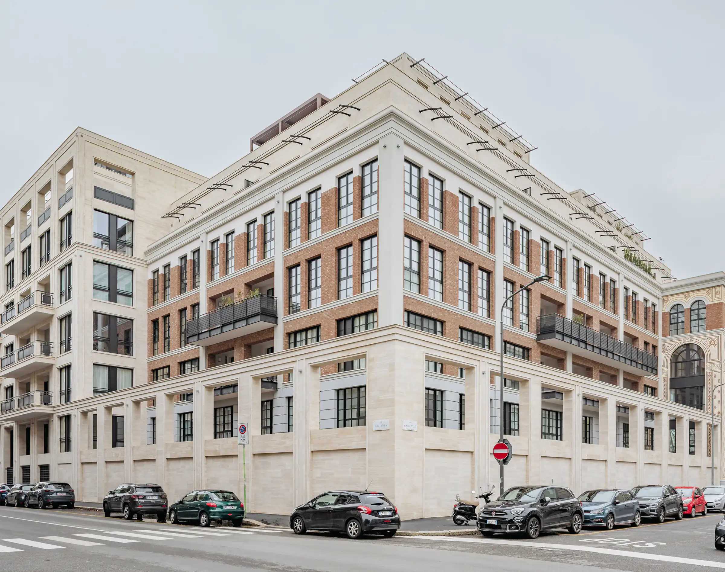 Vista angolare del Washington Building nel quartiere Washington di Milano: doppio prospetto con cornicioni in Travertino Romano, paramento in mattone rosso e piano attico con rivestimento in pietra - Trapattoni Marmi
