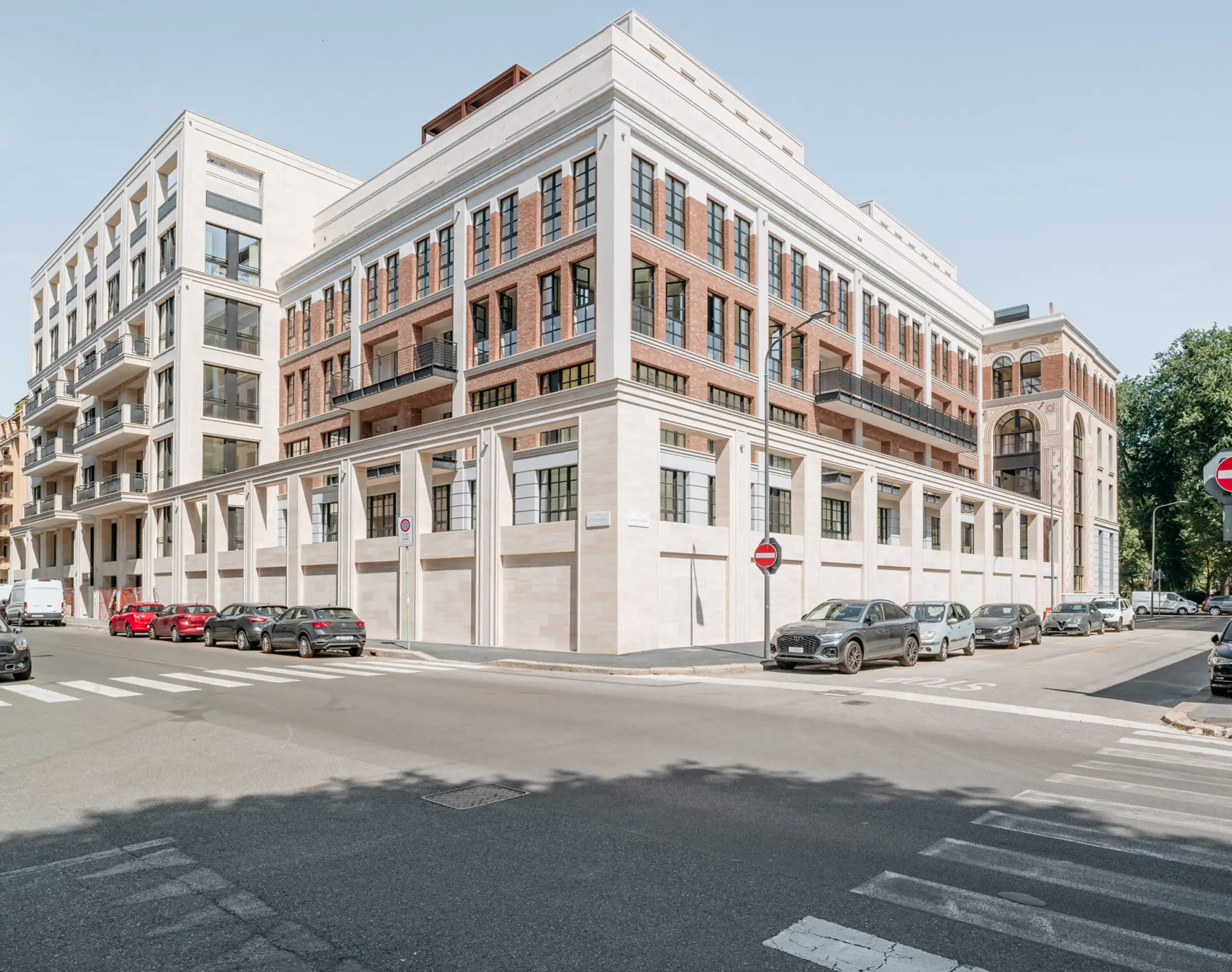 Vista stradale del Washington Building nel quartiere Washington di Milano: facciata con rivestimento in Travertino Romano al basamento, cornicioni decorativi in pietra e corpo in mattone a vista - fornitura e posa in opera Trapattoni Marmi