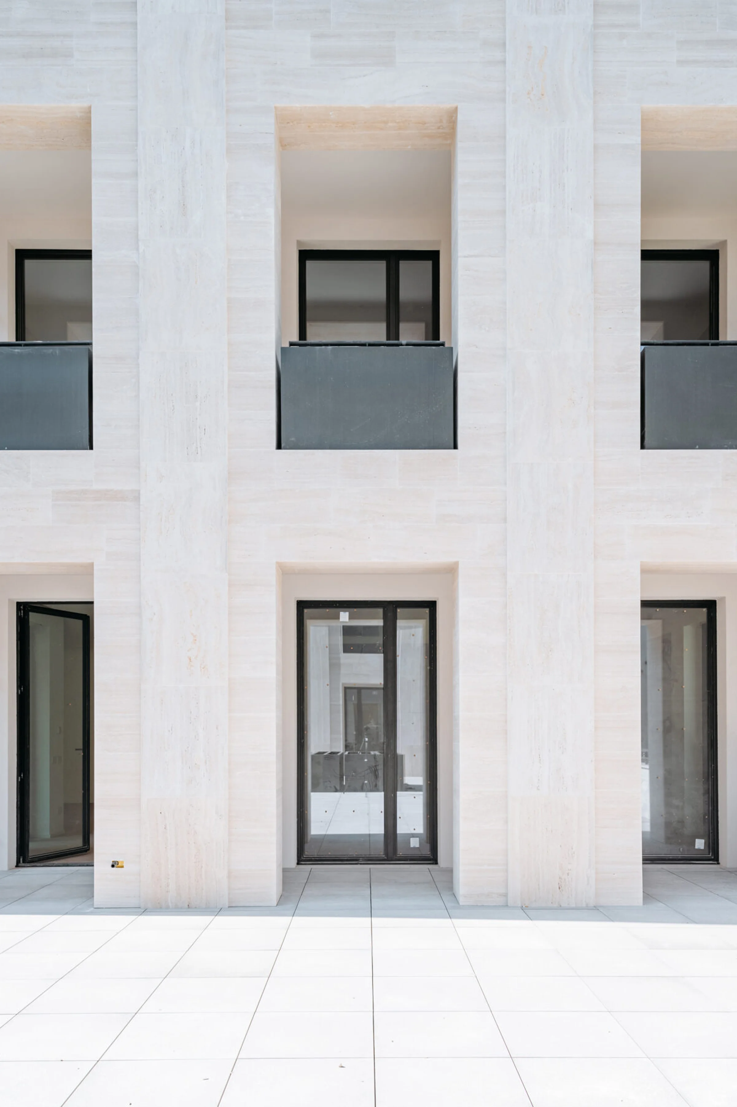 Cortile interno del Washington Building a Milano: pilastri e paraste in Travertino Romano con infissi neri a contrasto e pavimentazione in pietra chiara - riqualificazione di storica fabbrica nel quartiere Washington, posa in opera Trapattoni Marmi