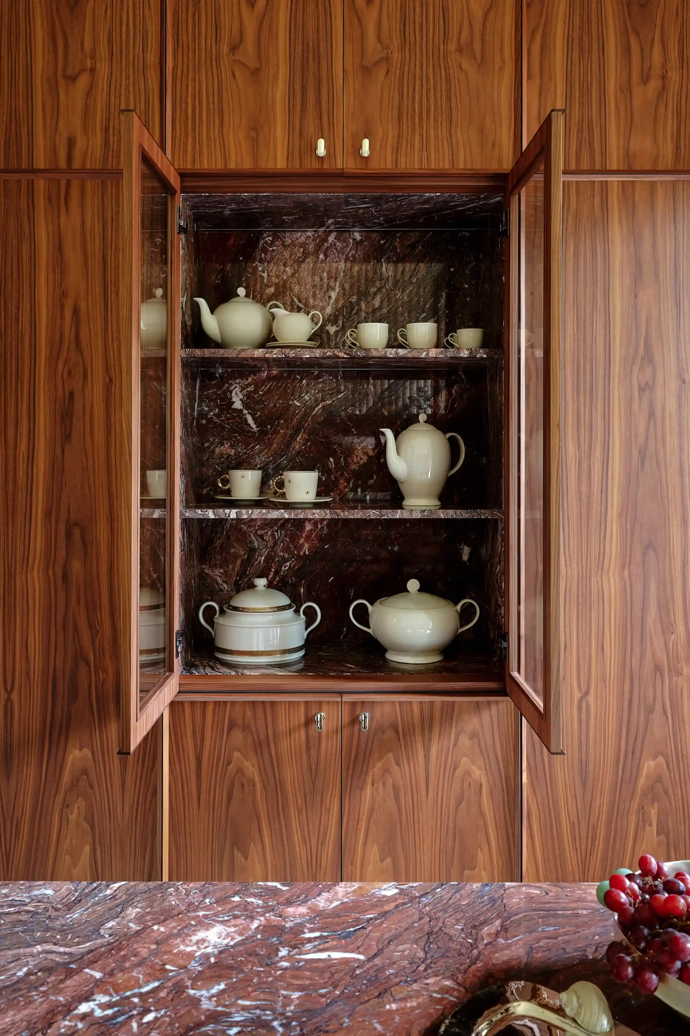 Armadio cucina in noce Canaletto aperto con interno rivestito in Cipollino rosso-viola e mensole in marmo, piano isola in Cipollino rosso-viola con decori e vasellame bianco - dimora ai Navigli di Milano, LC Atelier x Trapattoni Marmi